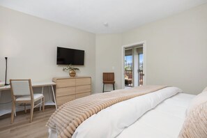 Ein Schlafzimmer mit einem Bett, einem Schreibtisch, einem Stuhl, einem Fernseher und Blick ins Freie.