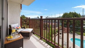 A balcony with wicker furniture, a tray with lemons and glasses, and a view of a swimming pool and greenery. - Condo on property at LaCosta Golf Resort & Spa with Pool 680 (Carlsbad)
