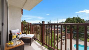 A balcony with wicker furniture, a tray with lemons and glasses, and a view of a swimming pool and greenery.