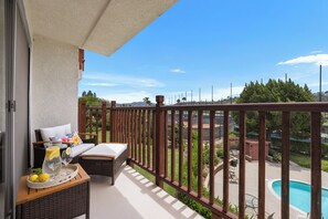 Ein Balkon mit Korbmöbeln, einer Ablage mit Zitronen und Gläsern sowie Blick auf einen Swimmingpool und viel Grün.