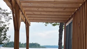 A wooden deck with stone flooring, overlooking a lake with a view of trees and rocks.