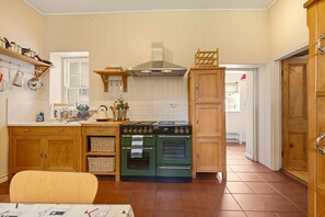 A kitchen with wooden cabinets, a stove, and a hanging rack. - Millhouse Cottage - North East Escapes (Waren Mill)