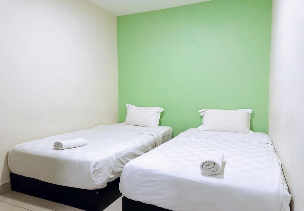Una habitación con dos camas individuales, cada una con colchón y almohada blancos, y una pared de acento verde.