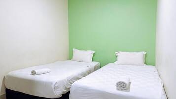 Una habitación con dos camas individuales, cada una con colchón y almohada blancos, y una pared de acento verde.