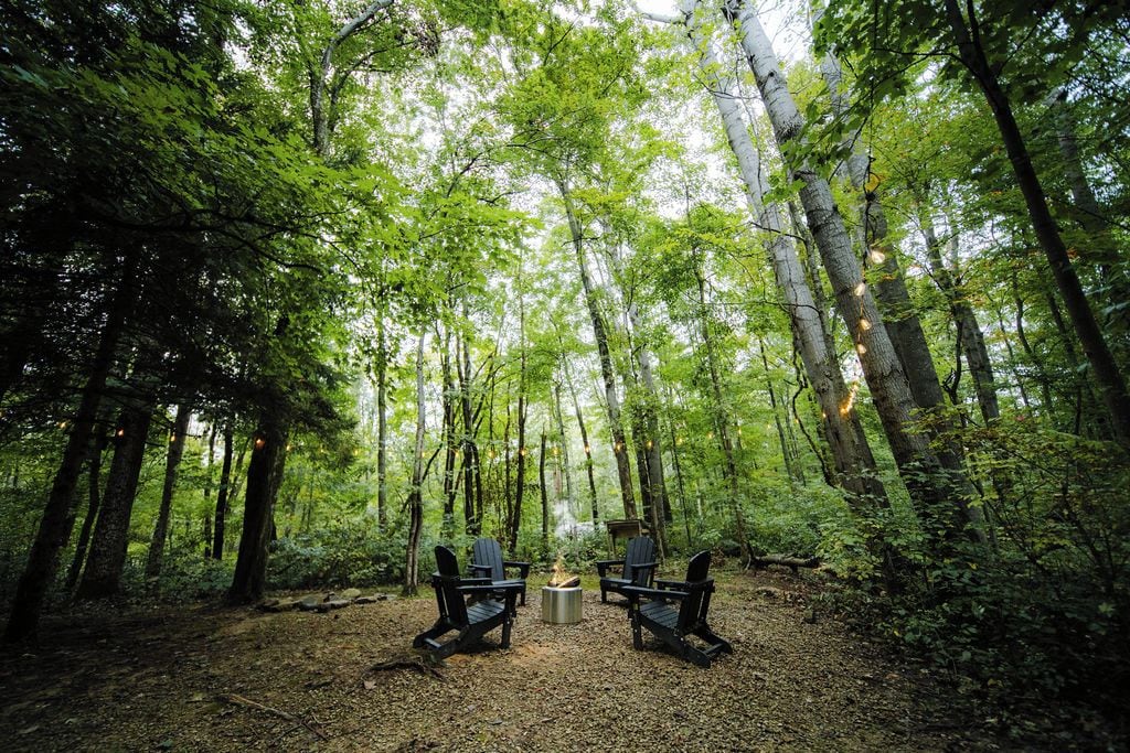 Une forêt avec deux fauteuils Adirondack placés face à un feu de camp.