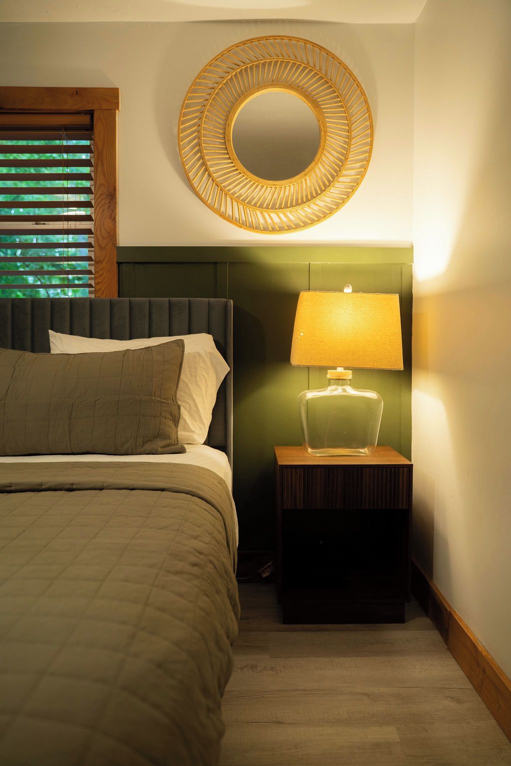 Ein Schlafzimmer mit einem Bett, einem Nachttisch mit Lampe und einem runden Wandspiegel.