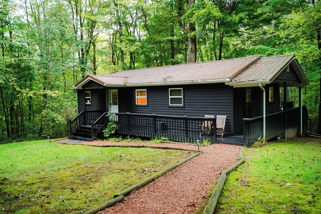 Un chalet rustique doté d’un porche, entouré d’une forêt dense.