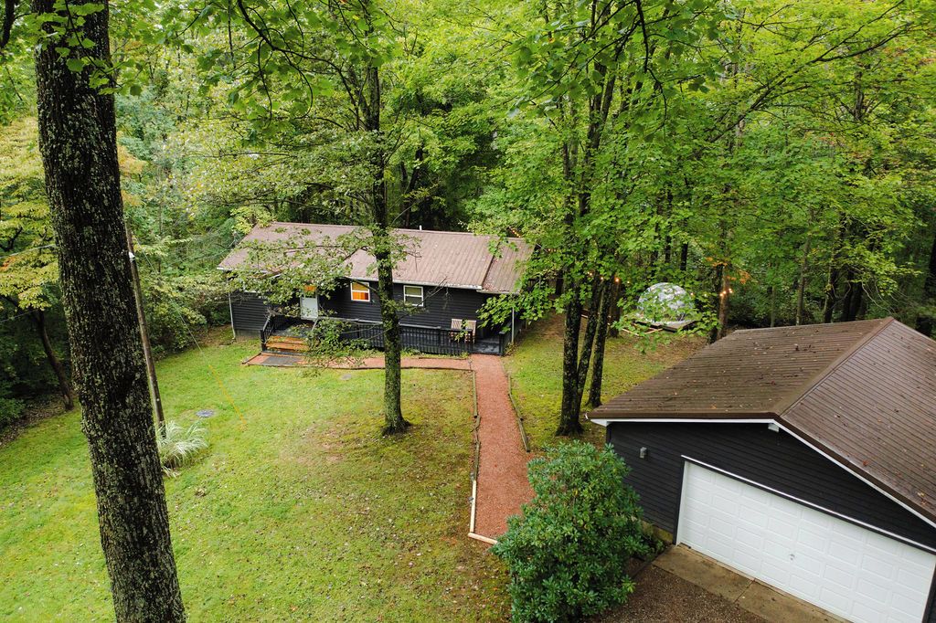 Une maison entourée d’arbres denses, avec un garage visible et un chemin menant à la maison.