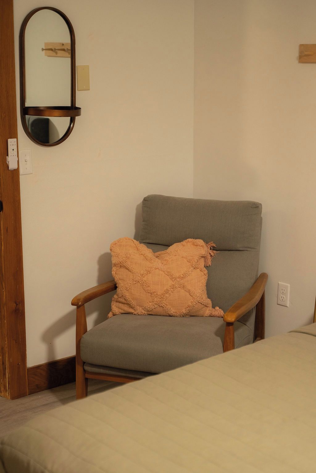 Een kamer met een houten stoel, een kussen, een spiegel en een bed.