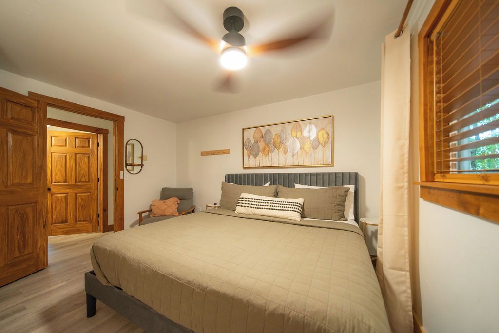 Une chambre avec un lit, un ventilateur de plafond, une fenêtre avec des stores et une porte.