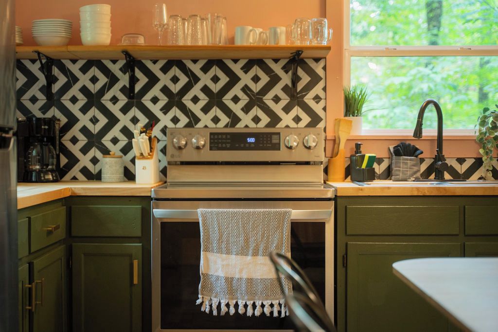 Une cuisine avec un mur de crédence à motifs, une cuisinière et une fenêtre donnant sur un paysage verdoyant.