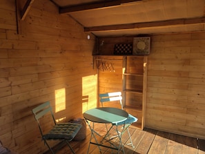 A wooden cabin interior with a table and chairs, a small shelf with a chessboard, and a window allowing sunlight to enter. - A cabin in a bamboo grove—a stunning natural setting (Miranda do Douro)