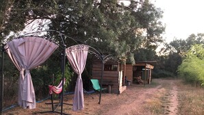 Une cabane en bois rustique, accessible par un sentier de terre, et entourée d’arbres.