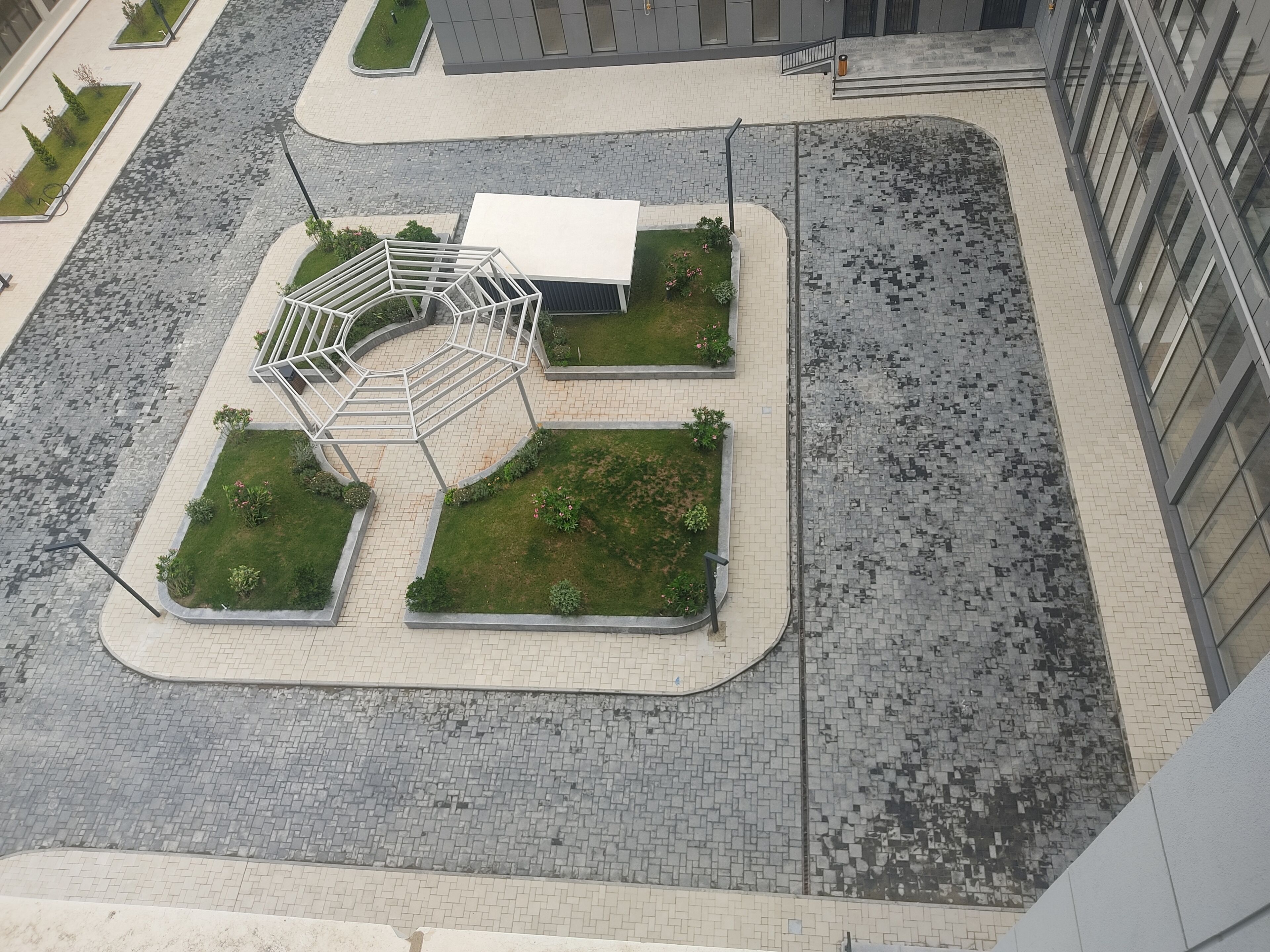En vy från ovan av ett parkliknande område med en central byggnad, omgivet av grönska och belagda gångvägar.