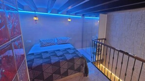 A bedroom with a bed, a patterned bedspread, a white pillow, a nightstand, and a wall-mounted lamp. - DUPLEX IN PALMA'S OLD TOWN (Palma)