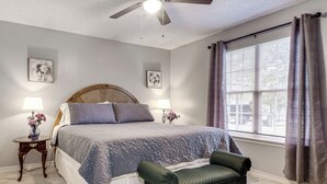 A bedroom with a bed, two bedside tables with lamps, a chair, a window with curtains, and a ceiling fan. - 2 Mi to Texas Tech: Pet-friendly Home, Fenced Yard (Lubbock)
