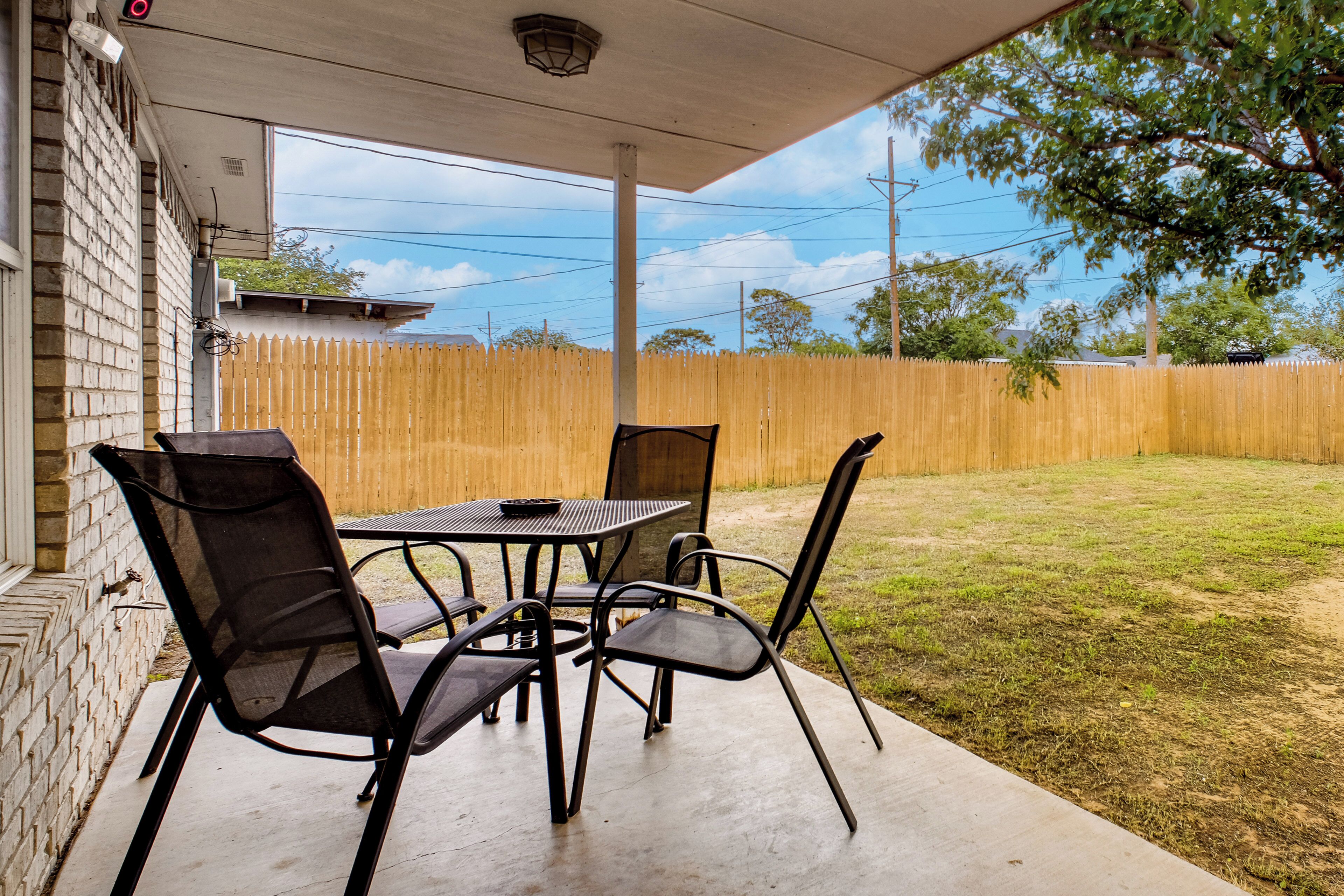An outdoor patio with a table and chairs, a wooden fence, and a grassy yard.