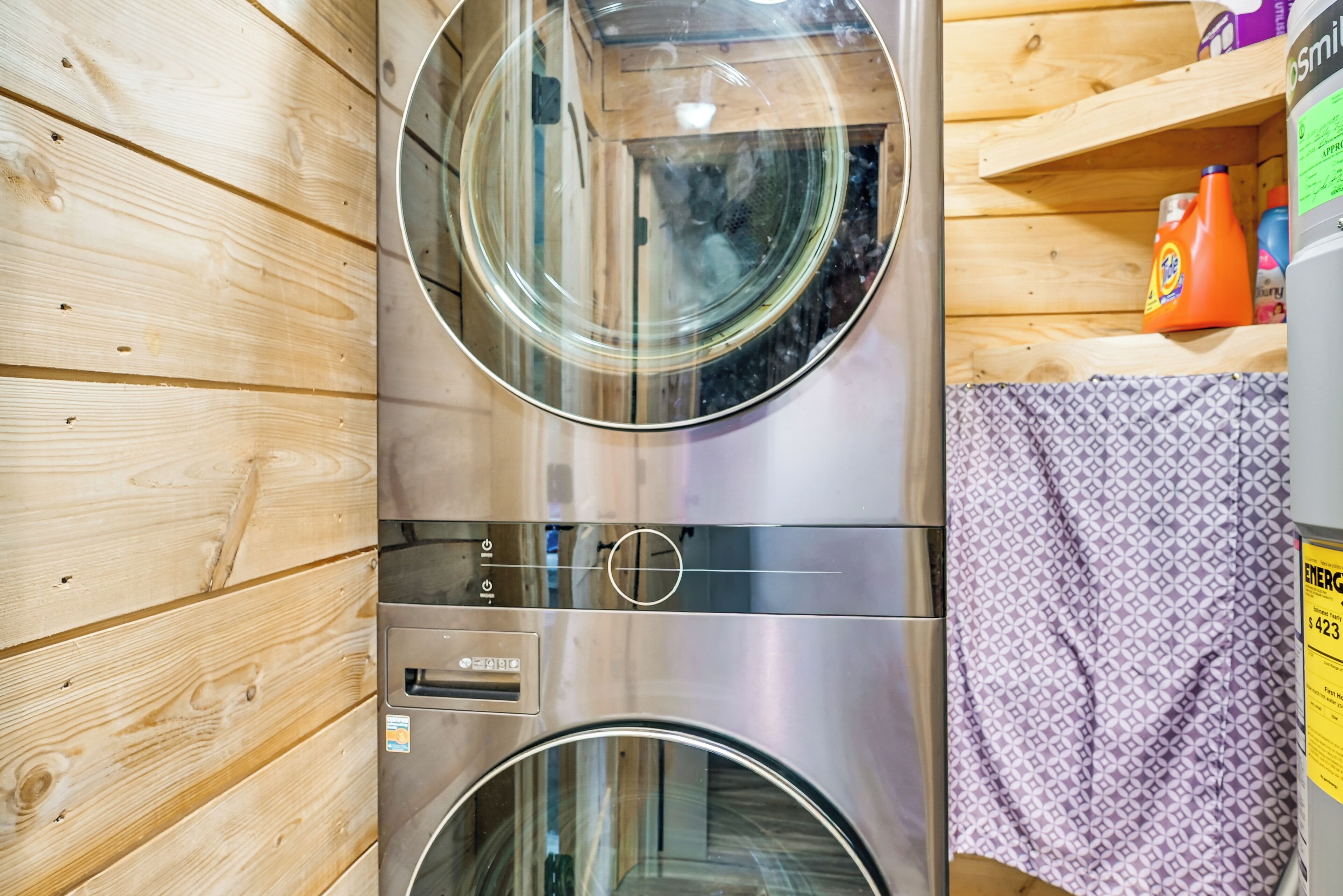 A laundry room with two stainless steel washers and dryers, wooden walls, and a shelf with cleaning supplies.