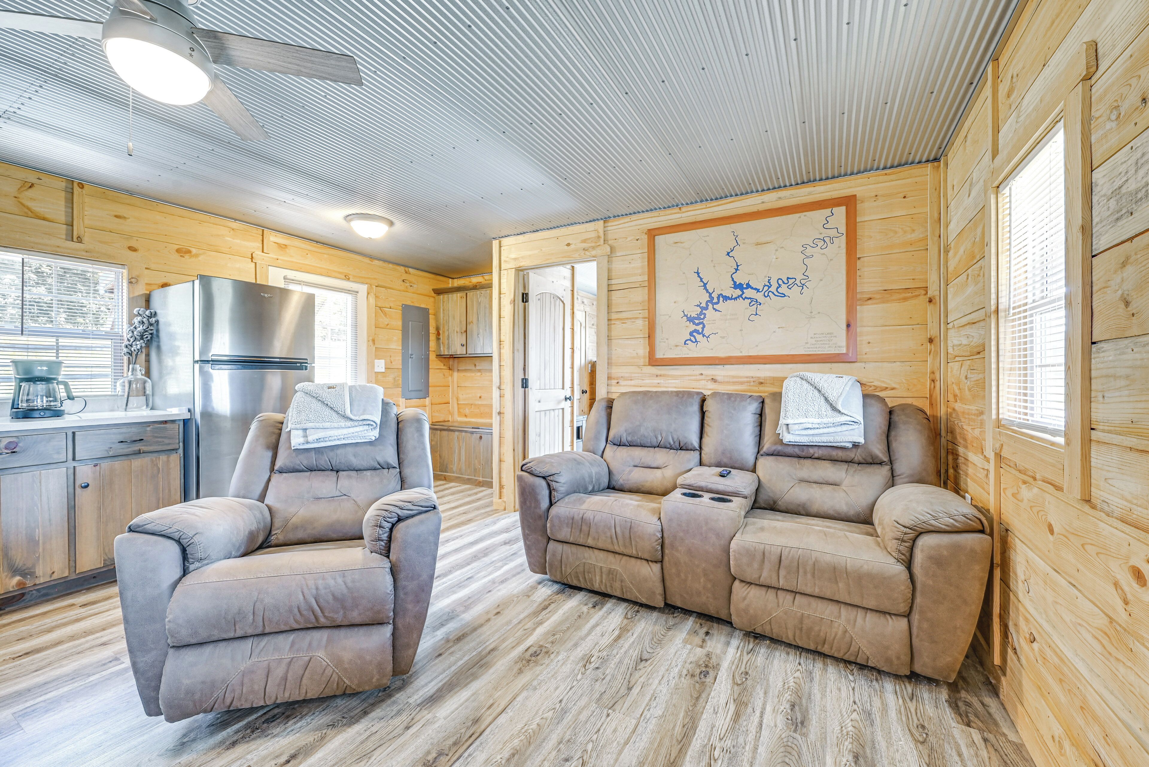 A cabin interior with a wooden interior, a kitchenette, a reclining sofa, and a ceiling fan.