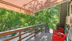 A wooden deck with a railing, a covered area with a beige canopy, and red chairs.