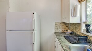 A kitchen with a white refrigerator, a granite countertop, a sink, and a window with a view of greenery.