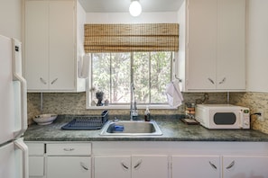 A kitchen with white cabinets, a window with a bamboo blind, a sink, a microwave, and a coffee maker.