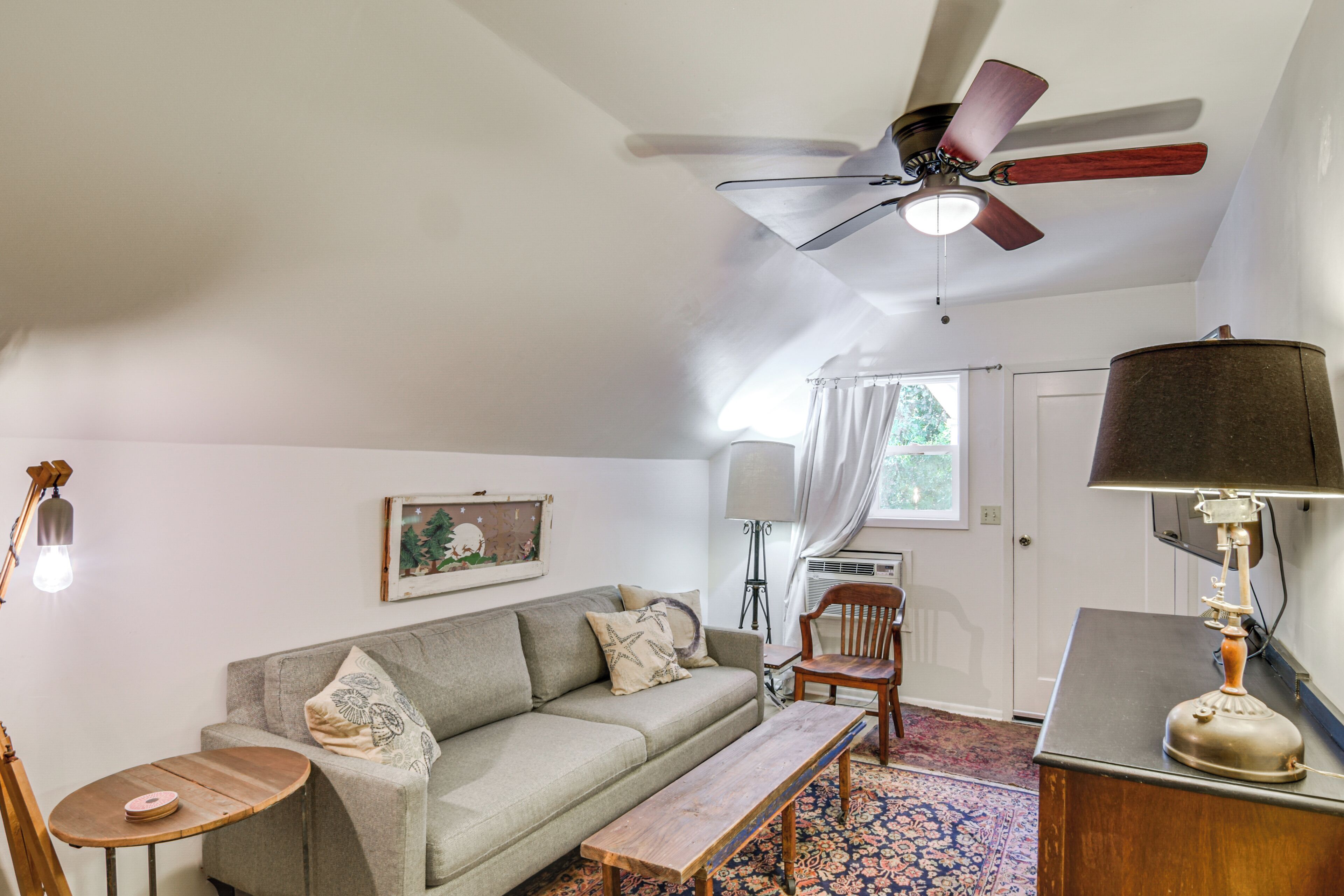 A living room with a ceiling fan, a sofa, a bench, a lamp, and a window with curtains.