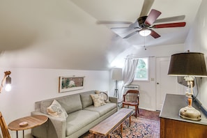 A living room with a ceiling fan, a sofa, a bench, a lamp, and a window with curtains.