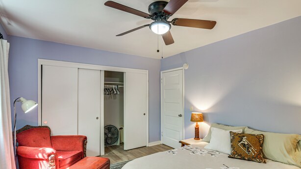 A bedroom with a bed, a red armchair, a ceiling fan, and a wardrobe.