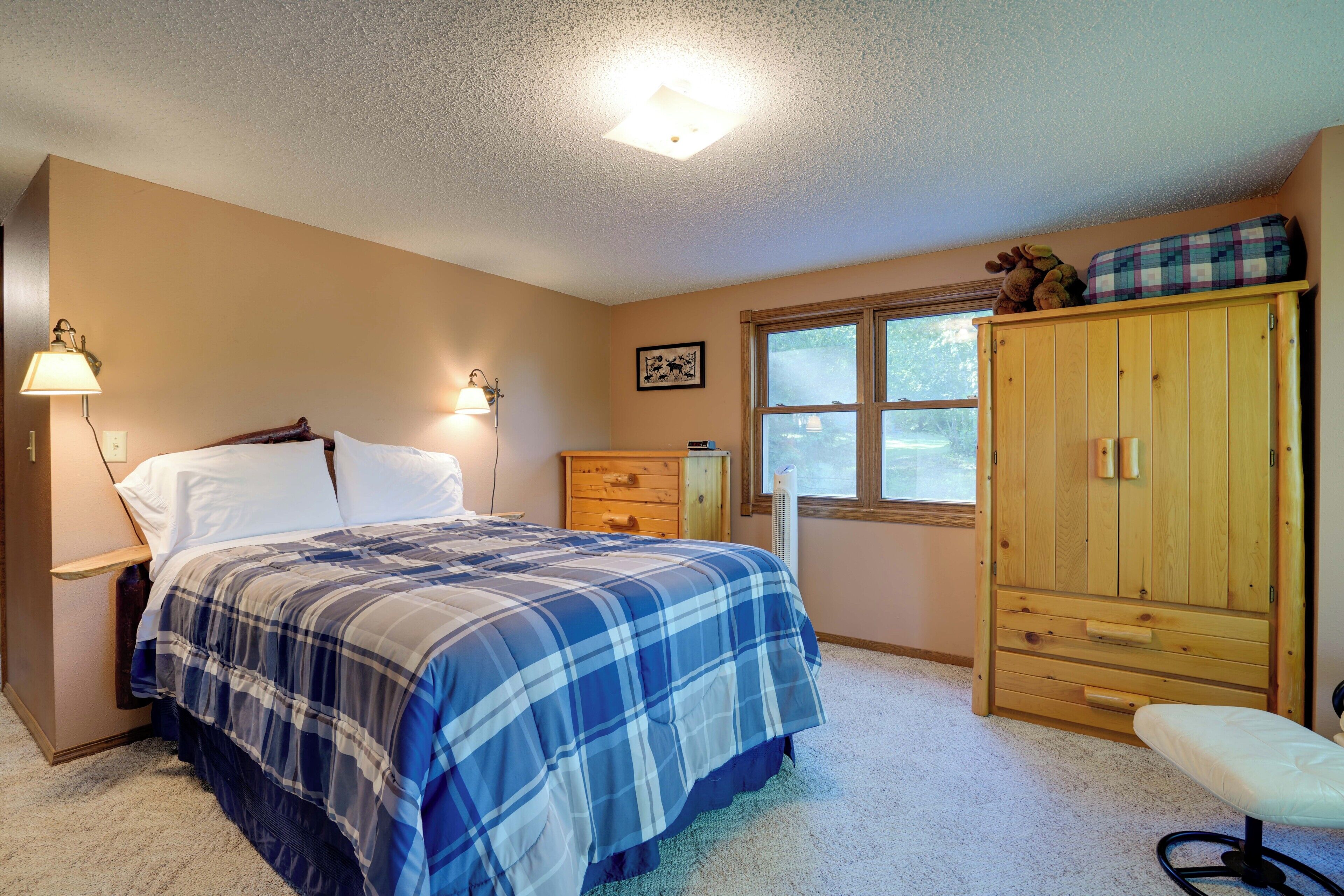 A bedroom with a bed, bedside lamps, a dresser, a window, and a bench.