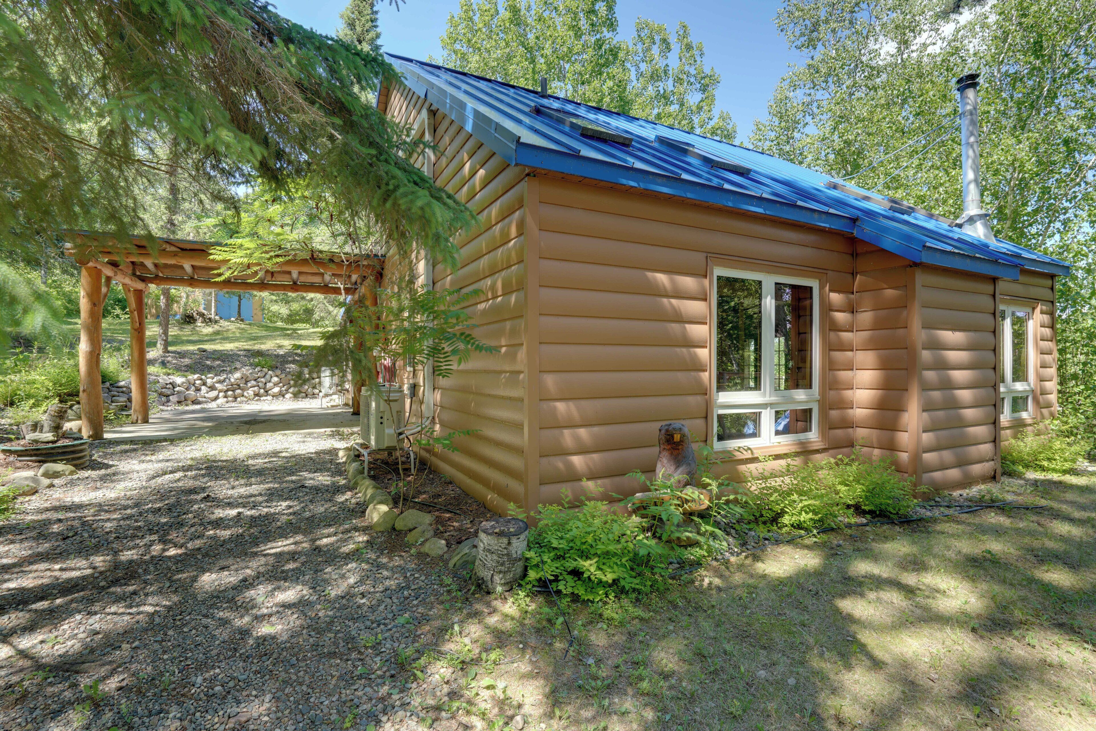 A wooden cabin with a blue roof, surrounded by trees and a stone wall.
