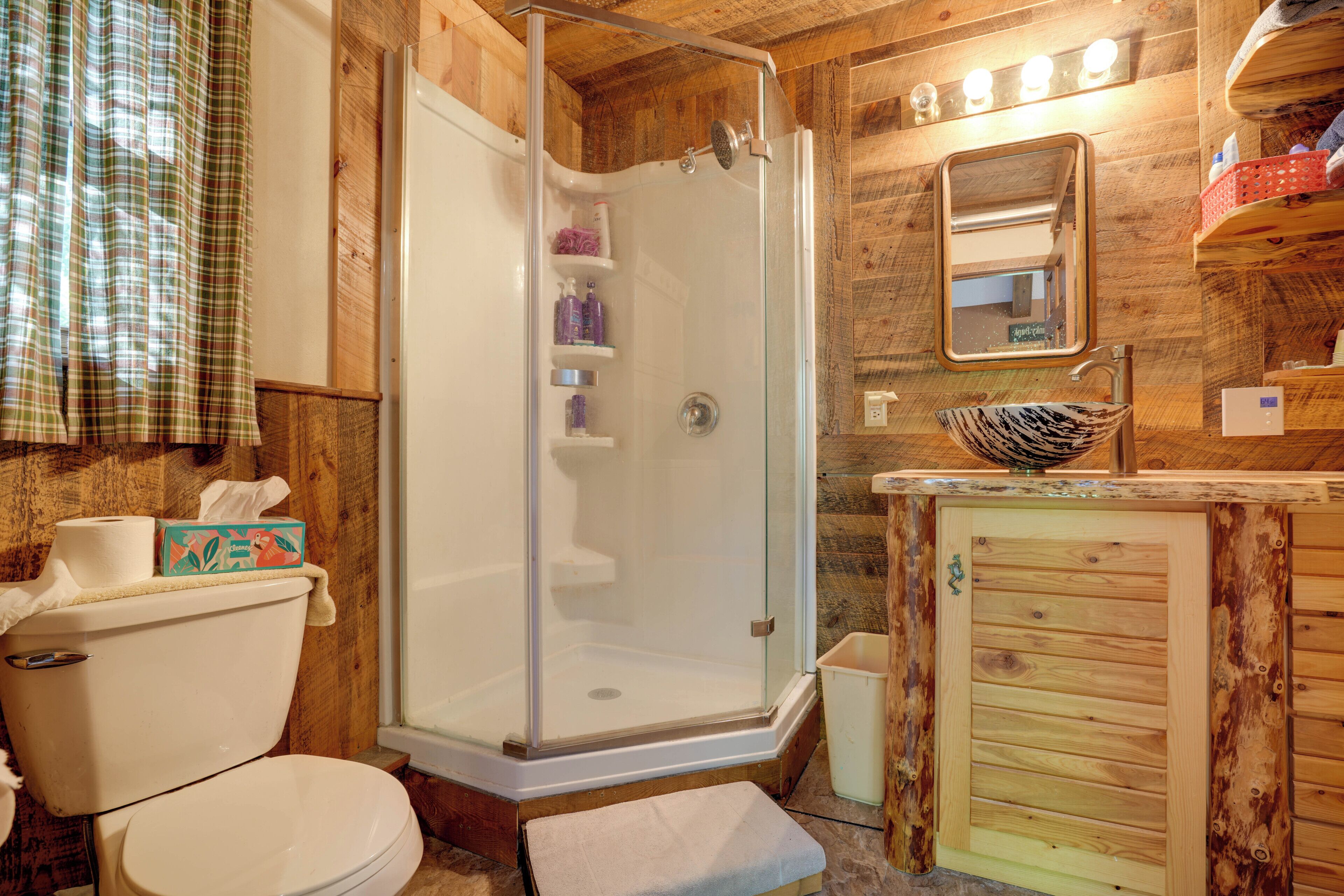 Een houten badkamer met een douche met glazen wanden, een toilet, een wastafel met houten kastje, en een spiegel boven de wastafel.