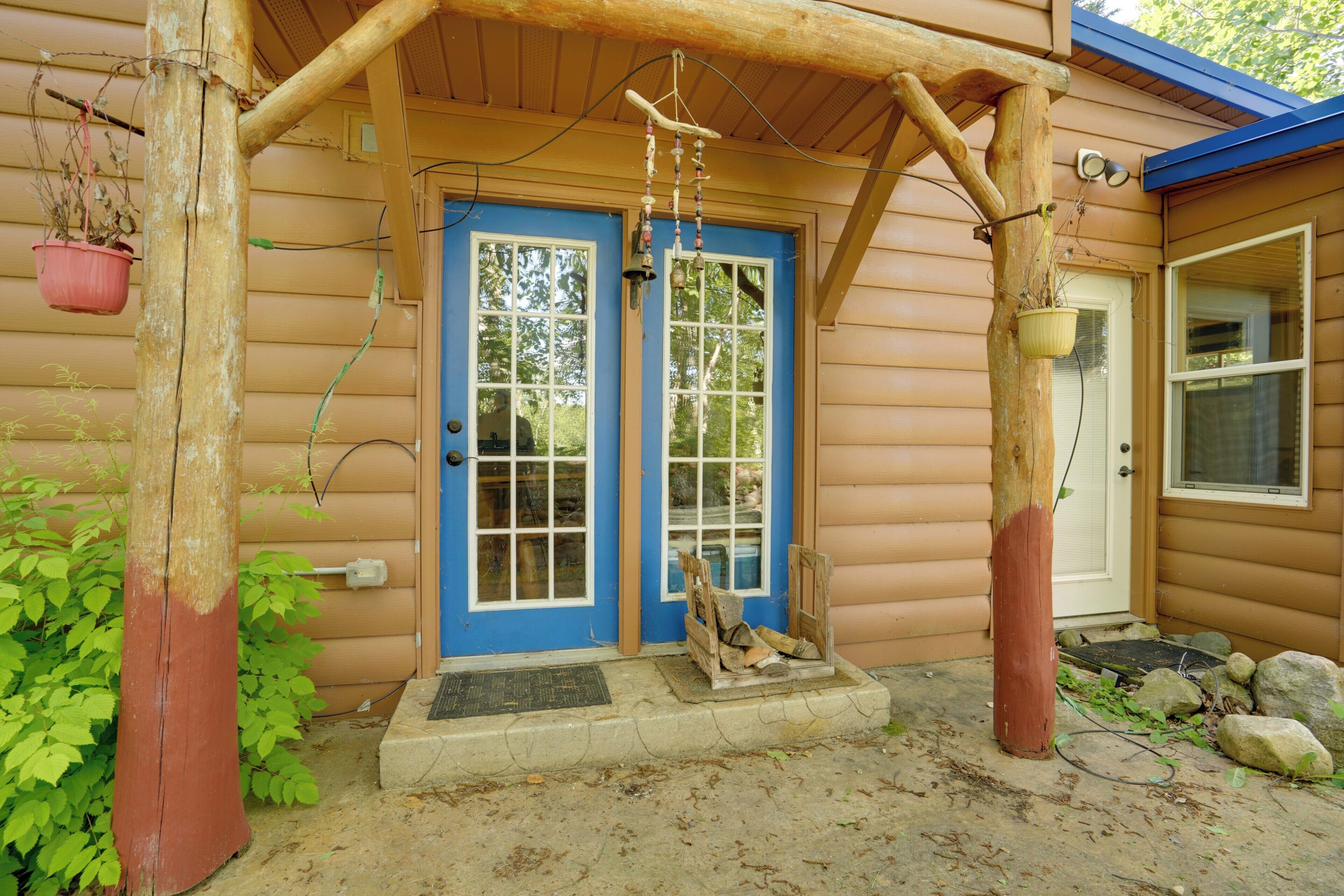 Une cabane en bois avec une porte bleue, une véranda avec une balançoire et une plante suspendue.