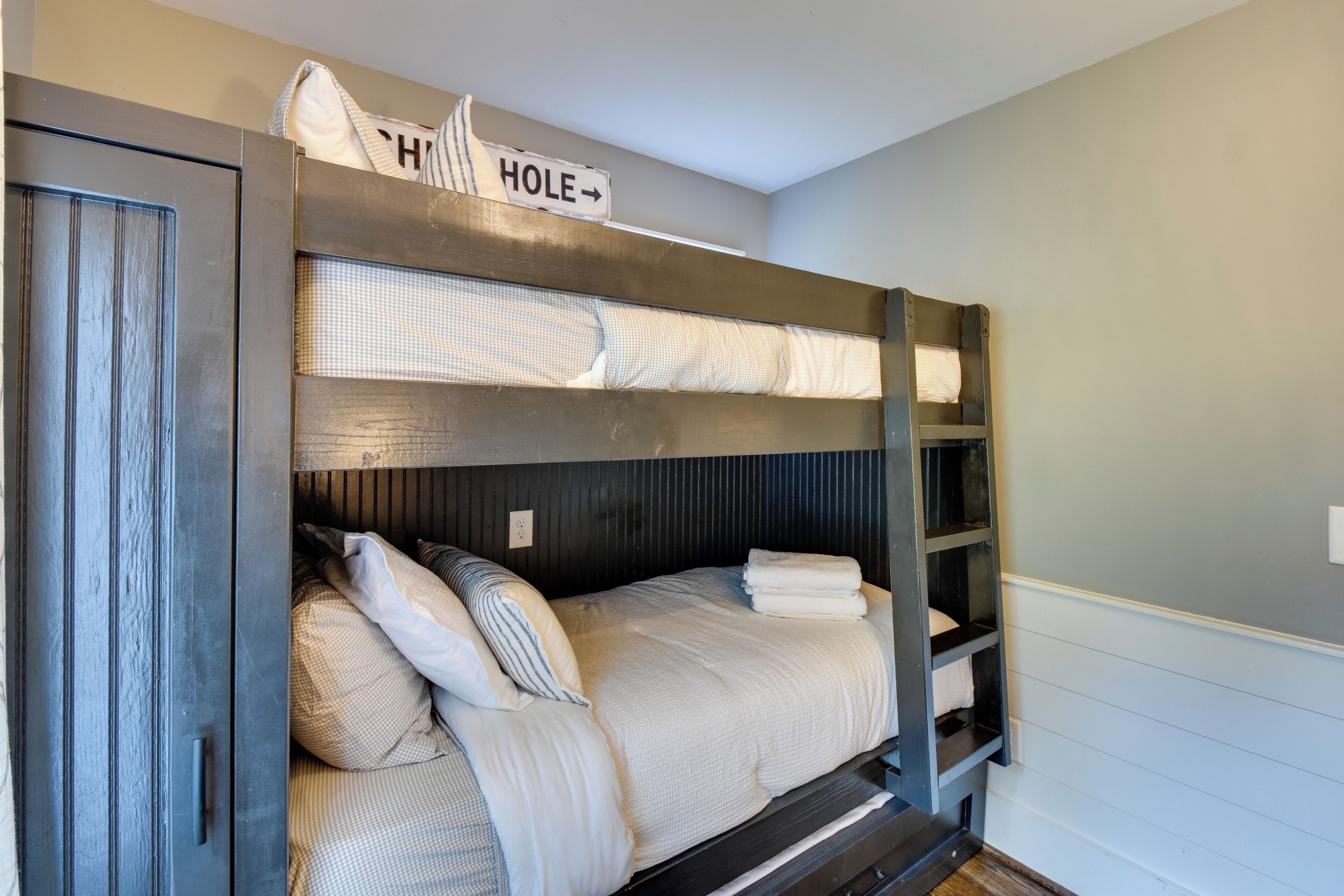 Una cama litera con cabecera que dice 'HOLE' y una pequeña estantería a la derecha.