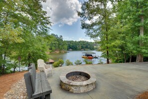 A stone fire pit surrounded by a deck, overlooking a lake with a dock and boat. - Waterfront Lake Keowee Home w/ Hot Tub & Views! (West Union)