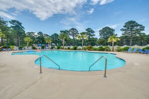 Ein Swimmingpool mit weißem Zaun, umgeben von Palmen und blauen Liegestühlen.