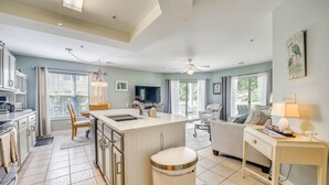 A modern kitchen with a central island, a dining area with a sofa, and a living room with a television. - Gorgeous Ground Floor Condo Just Steps to Pool! (Calabash)