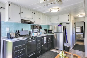 A compact kitchen with white cabinets, a gas stove, a microwave, and a refrigerator. - Fish, Hunt & Explore! Mtn-view Tiny Home in Noxon (Noxon)