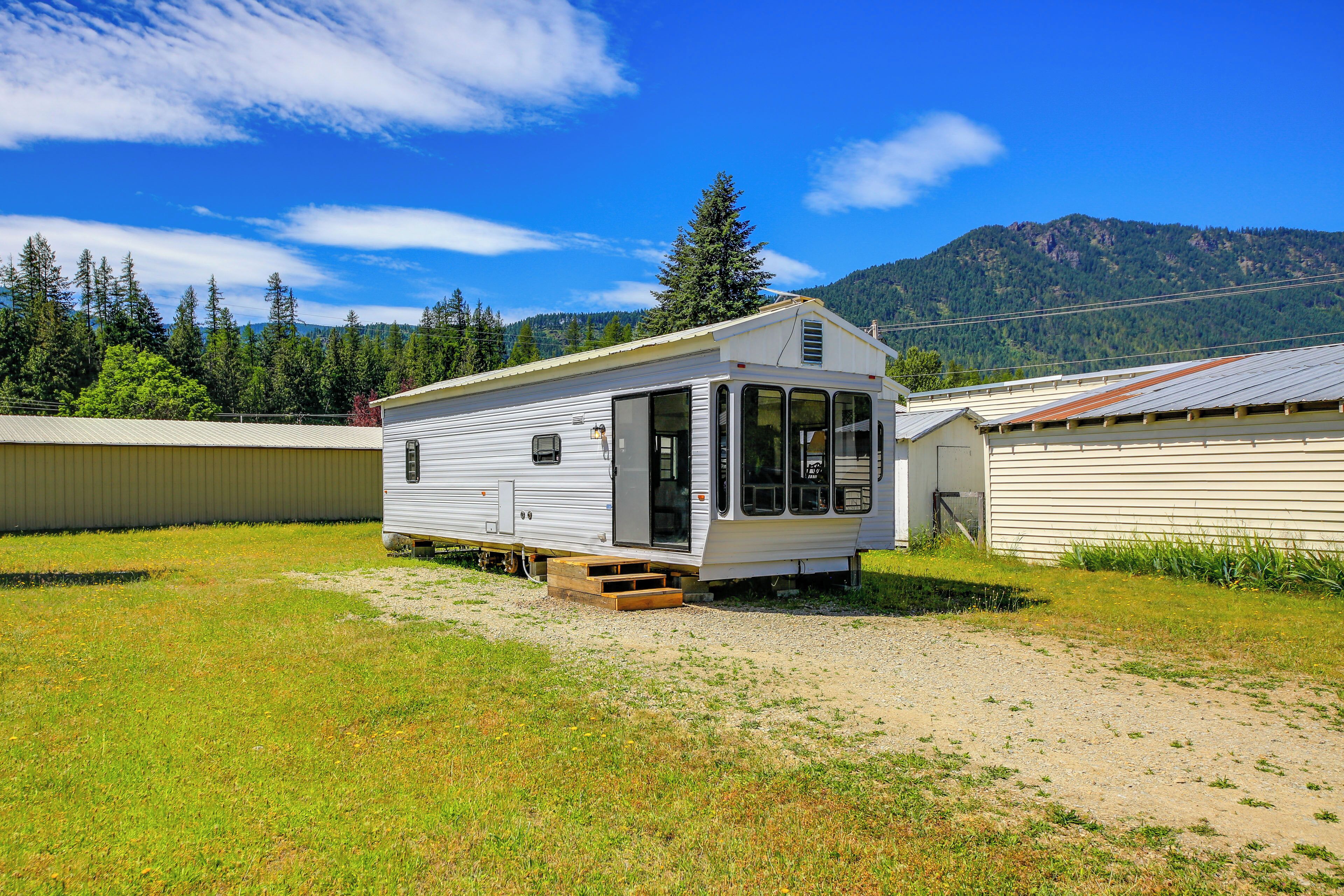 A mobile home with a covered porch, a small entryway, and a gravel driveway.