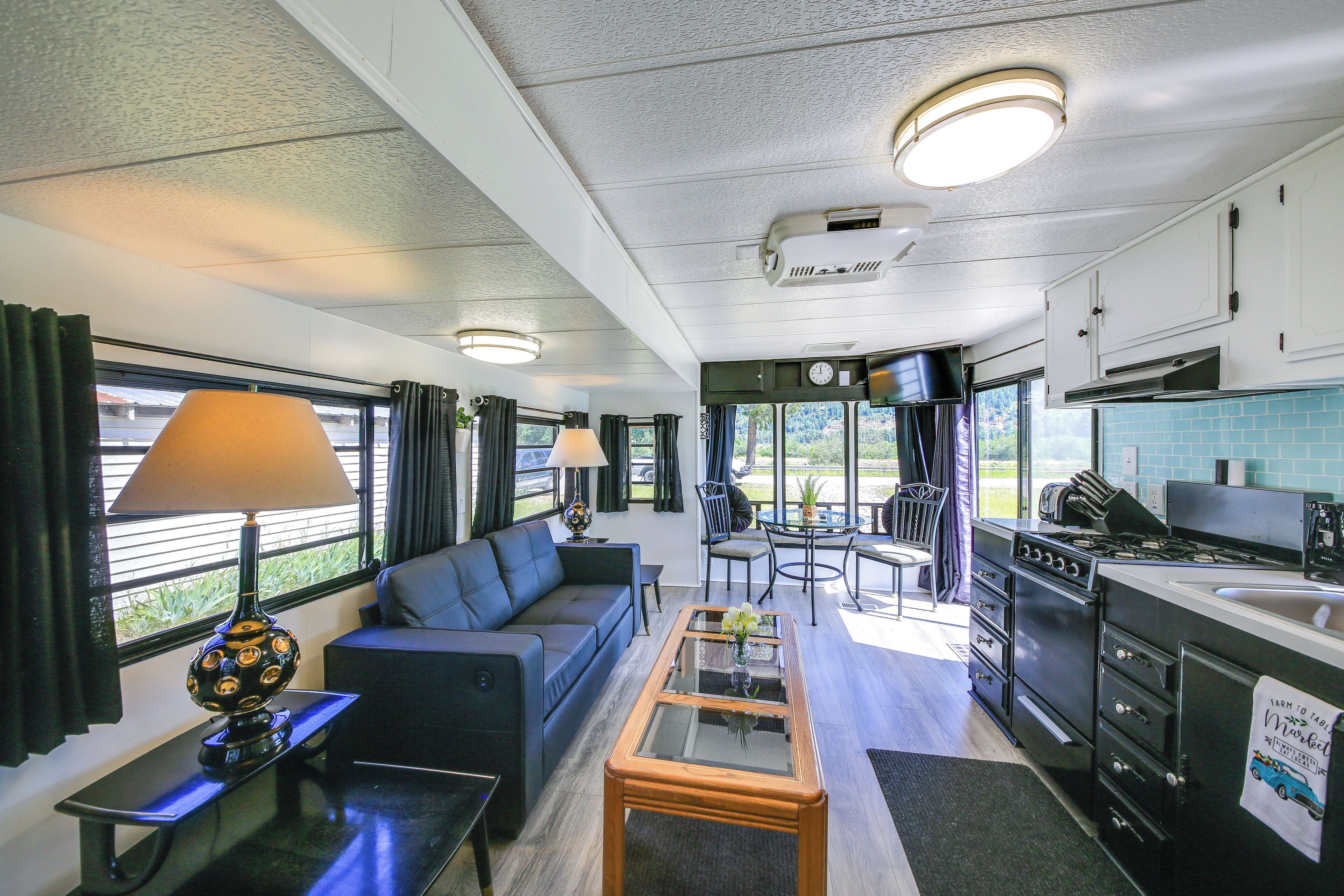 A compact living space with a sofa, coffee table, dining table, kitchen area, and large windows.