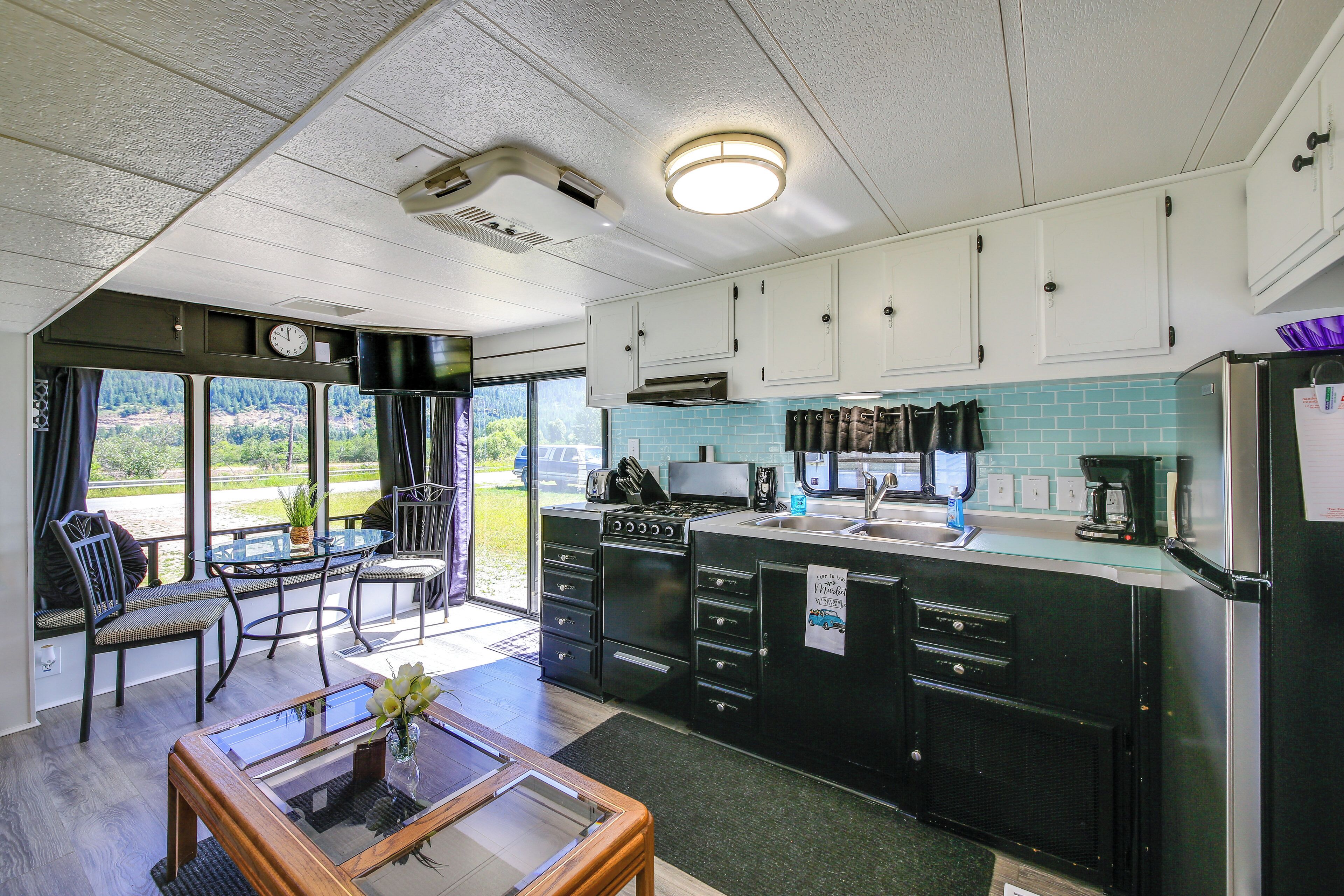 A compact kitchen with a dining area, a view through the window, and a clock on the wall.