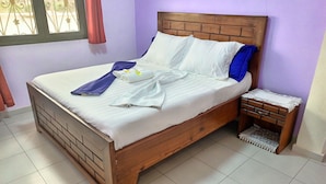 A bed with white linens, a wooden headboard, and a nightstand with a lace-trimmed tablecloth.