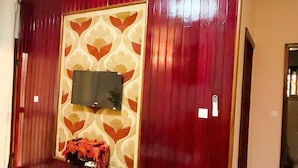A living room with a flat-screen TV mounted on a red panel, a dining table with a white tablecloth, and a patterned rug.