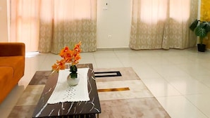 A living room with a sofa, a coffee table with a vase of flowers, a ceiling light, and a door with an air conditioning unit.