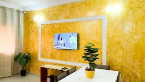 A dining area with a table set for two, a television mounted on the wall, and a potted plant on the table.