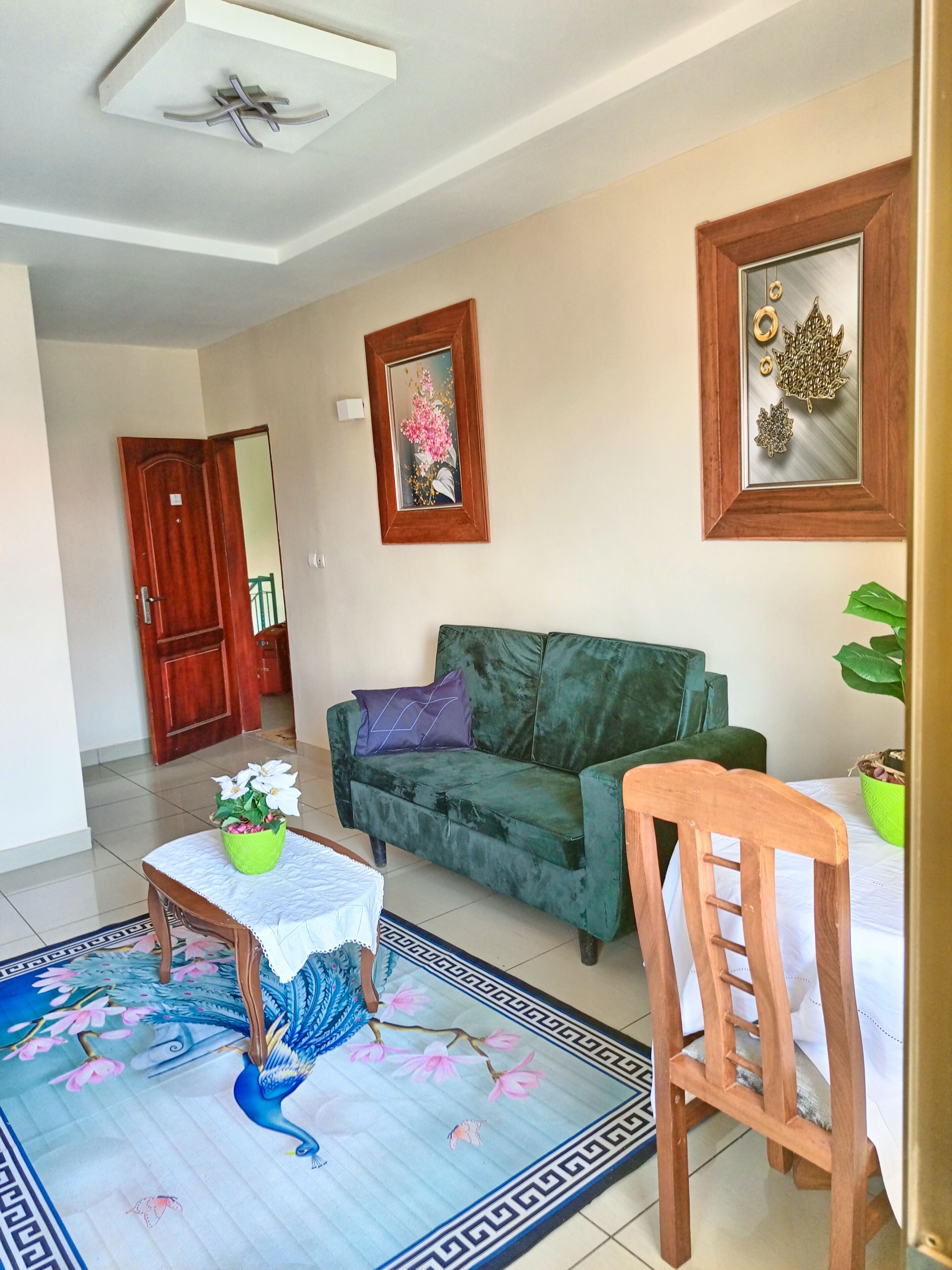 Uma sala de estar com um sofá verde, uma cadeira de madeira, uma mesa pequena com uma planta e um espelho decorativo na parede.