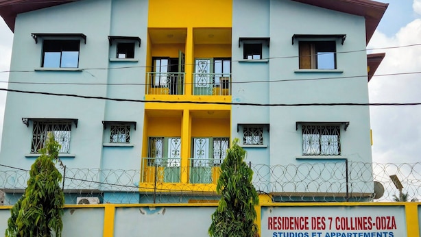 A multi-story building with a yellow and blue facade, featuring balconies and barred windows.