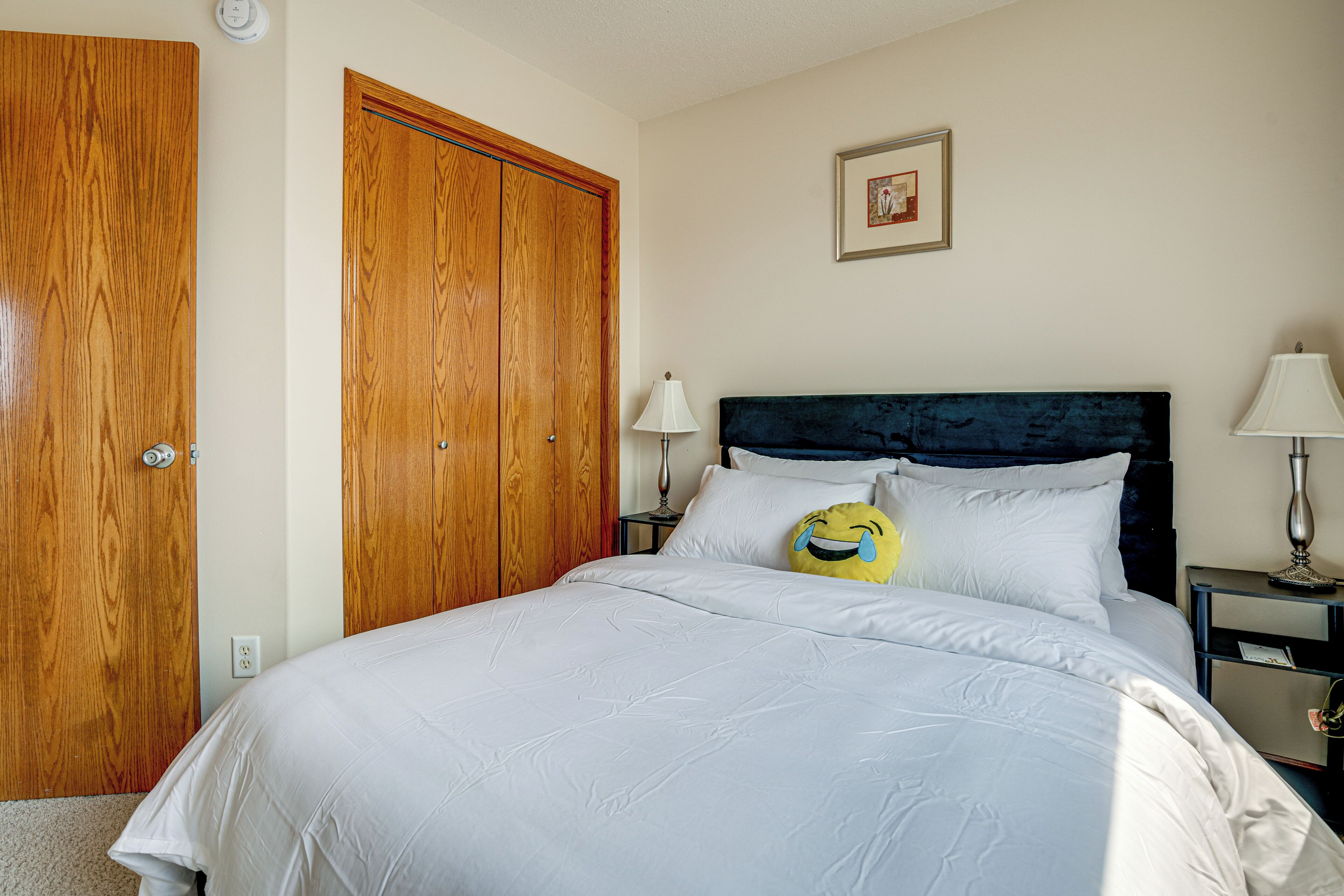 Ein Schlafzimmer mit Bett, Holzschrank, Nachttischen und einem an der Wand hängenden Bild.
