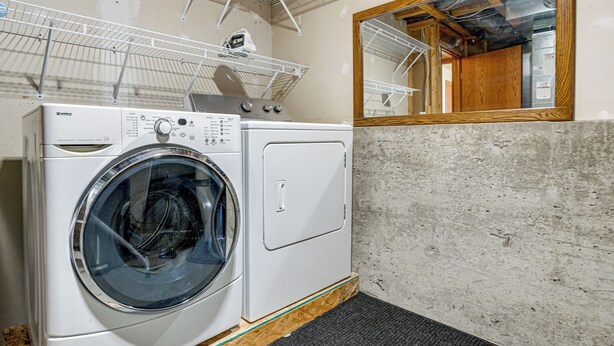 A laundry area with a washing machine and dryer, a metal shelf, and a mirror.