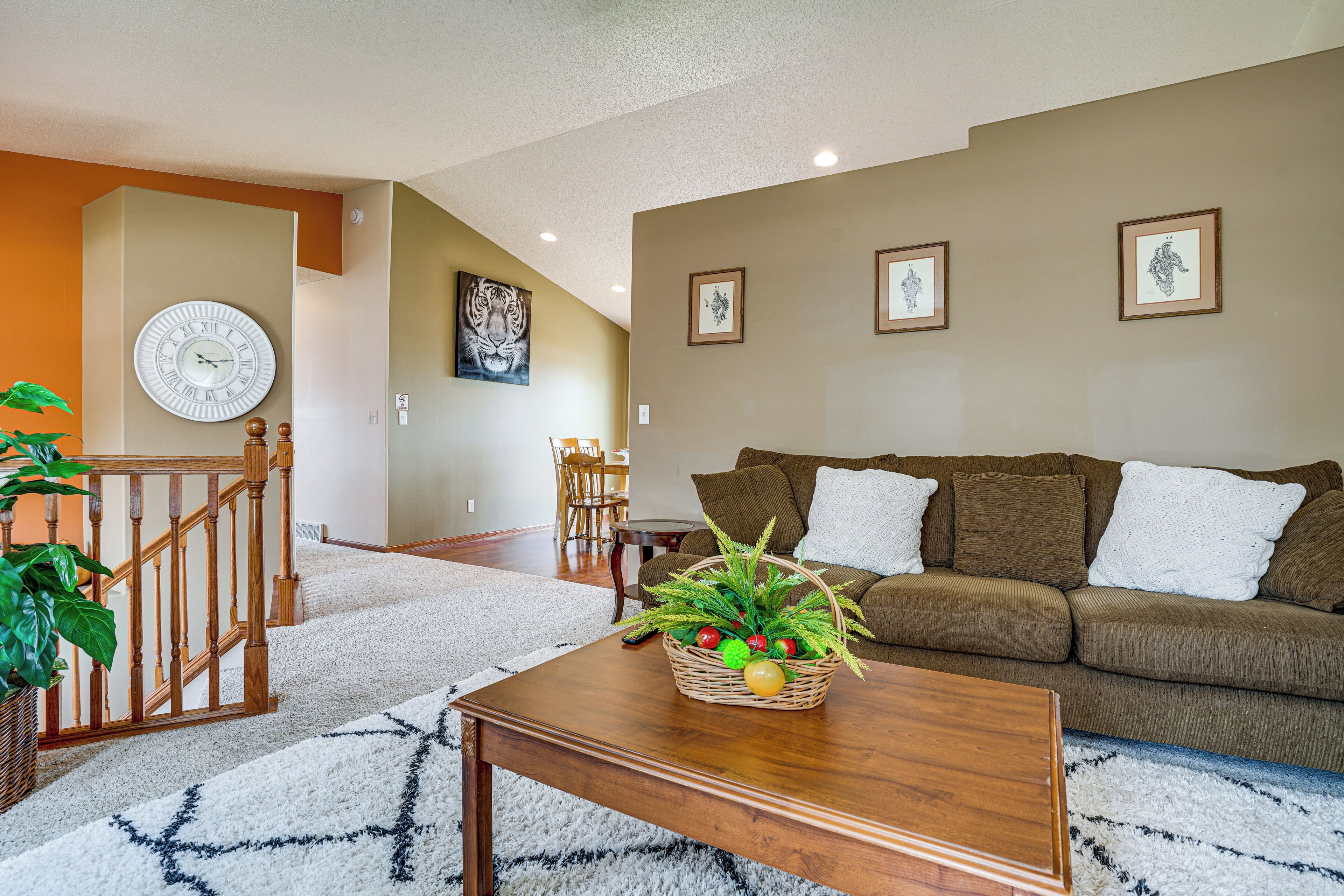 A living room with a wooden coffee table, a brown sofa, a white clock, and framed artwork on the wall.